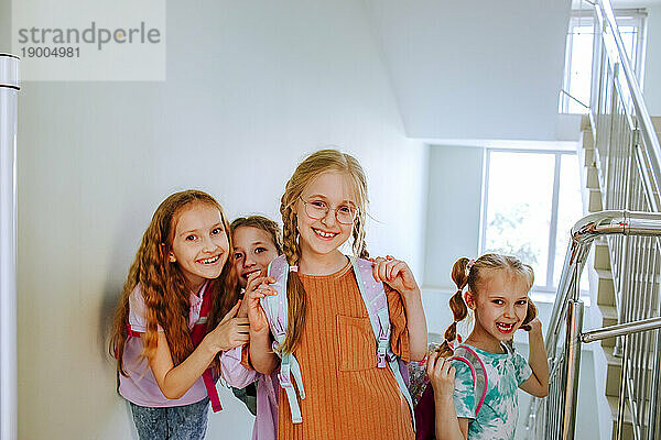 Lächelnde Schulmädchen mit Rucksack stehen am Schultreppenhaus
