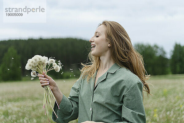 Smiling young woman holding dandelions on field