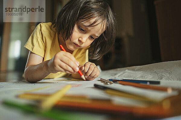 Konzentrierter Junge zeichnet zu Hause mit Buntstift