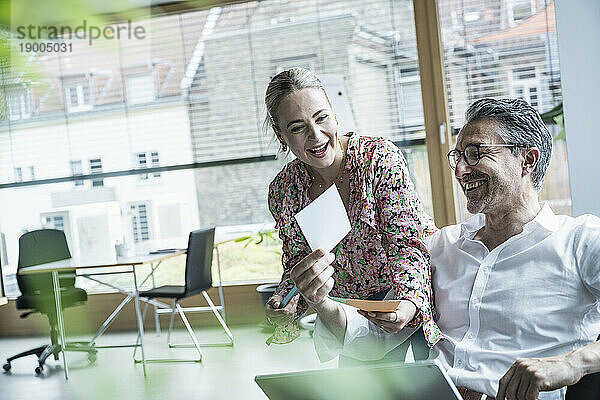 Glückliche Geschäftsfrau und Geschäftsmann lachen über Foto im Büro