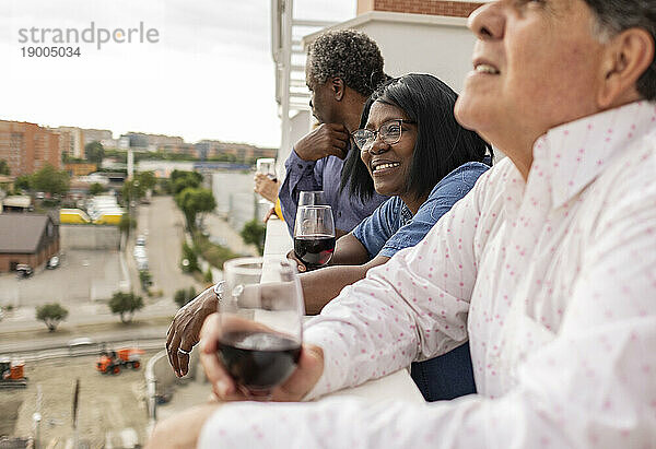 Lächelnde Seniorin genießt Drinks mit Freunden auf dem Balkon