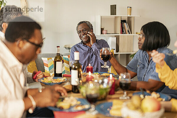 Glücklicher älterer Mann  der mit Freunden beim Essen auf der Dinnerparty lacht