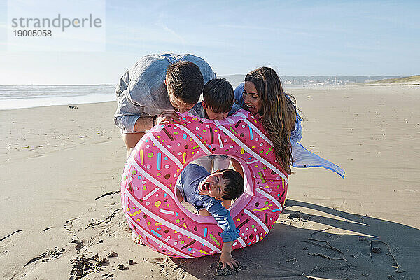 Playful family with pink doughnut shaped inflatable ring at beach