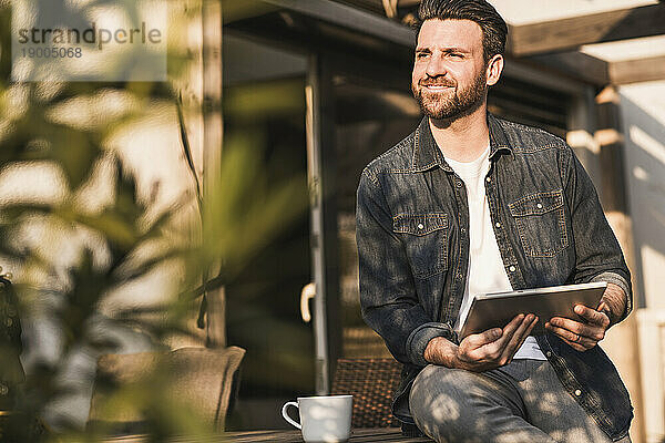 Lächelnder Mann sitzt an einem sonnigen Tag mit einem Tablet-PC