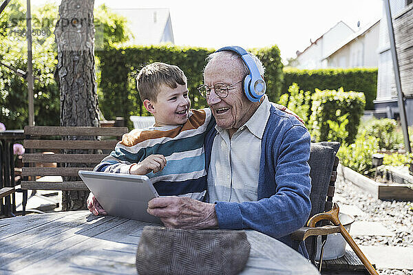 Glücklicher Junge mit Großvater  der kabellose Kopfhörer trägt und einen Tablet-PC benutzt