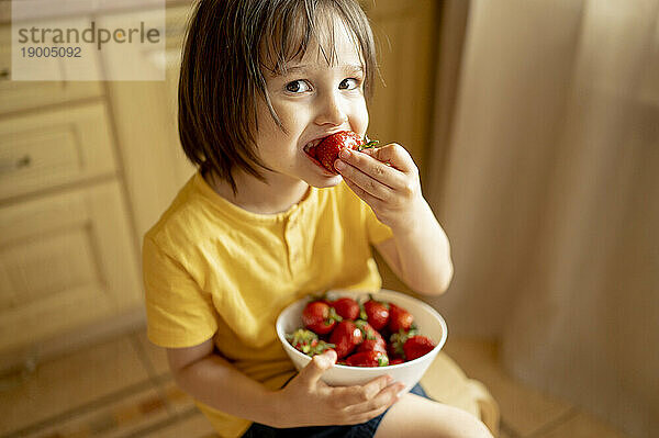 Lächelnder Junge  der zu Hause Erdbeeren aus einer Schüssel isst