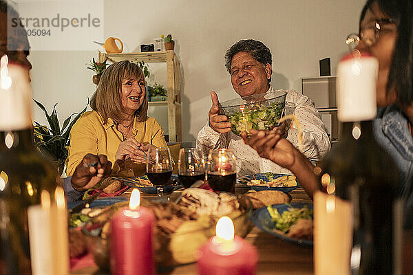 Glückliche ältere Freunde genießen das Abendessen mit Kerzen auf dem heimischen Tisch