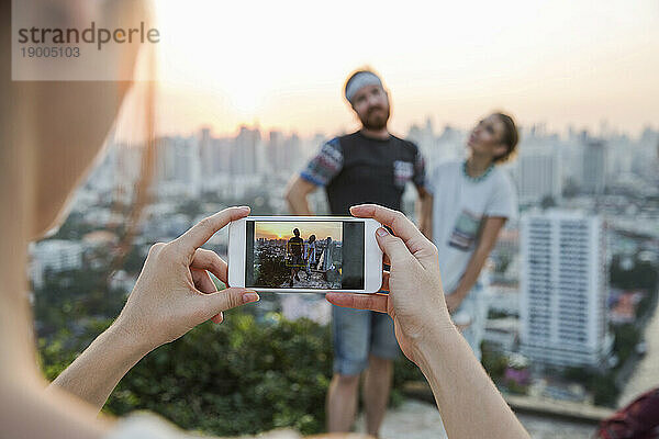 Frau fotografiert Paar mit Smartphone bei Sonnenuntergang in der Stadt