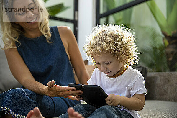 Lächelnde Frau zeigt ihrem Sohn zu Hause einen Tablet-PC