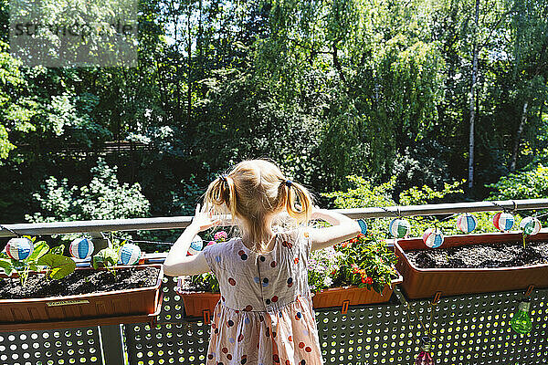 Girl standing near plants in balcony at sunny day