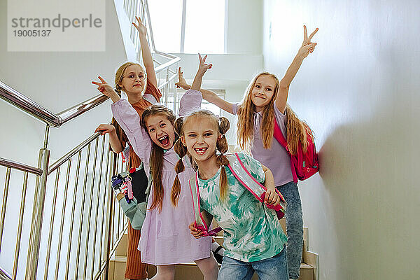 Lächelnde Schulmädchen stehen mit erhobener Hand auf der Schultreppe