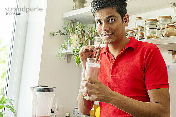 Lächelnder Mann hält Smoothie-Glas zu Hause