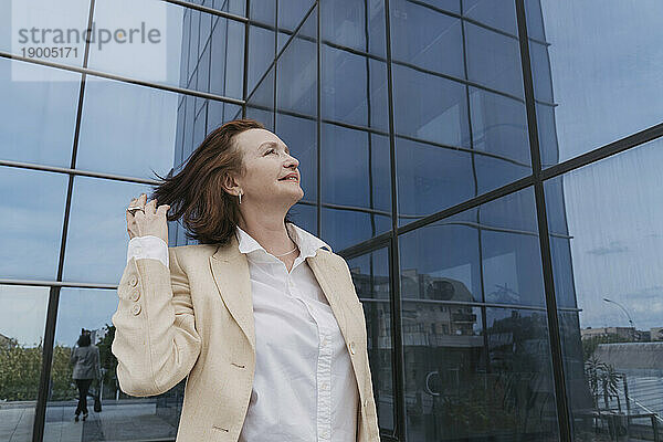 Nachdenkliche Geschäftsfrau mit der Hand im Haar in der Nähe eines Bürogebäudes