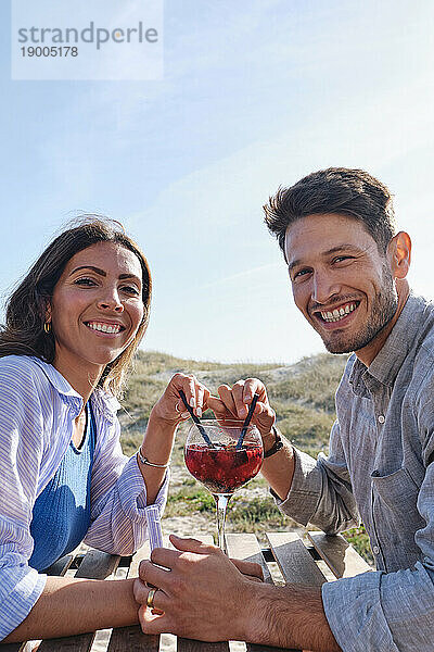 Glückliches Paar genießt Drink am Tisch am Strand