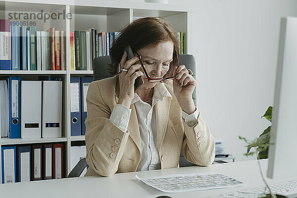 Ältere Geschäftsfrau telefoniert am Tisch im Büro