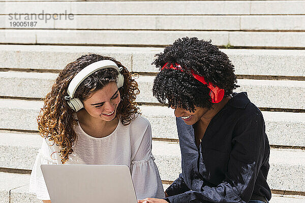 Freunde tragen an einem sonnigen Tag gemeinsam kabellose Kopfhörer und nutzen ihren Laptop