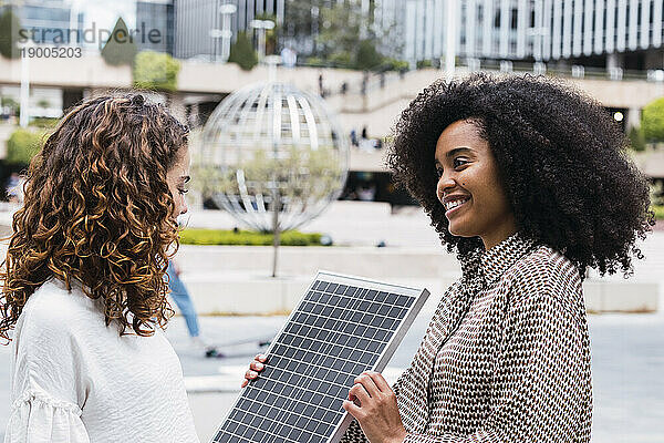 Glückliche Geschäftsfrau zeigt einem Kollegen im Büropark Solarpanel