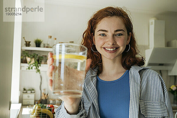 Glückliche rothaarige Frau mit einem Glas Wasser zu Hause