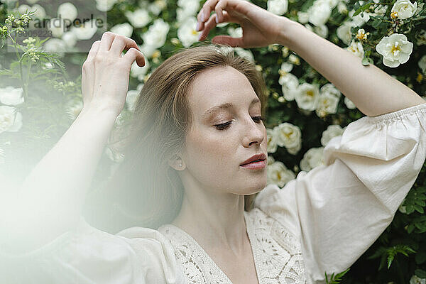 Junge Frau mit erhobenen Armen durch weißen Blumenstrauch