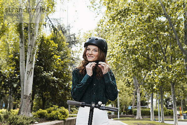 Glückliche junge Frau passt Helm im Park an