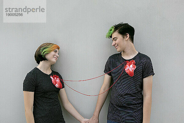Teenage couple connected with hearts in front of gray background