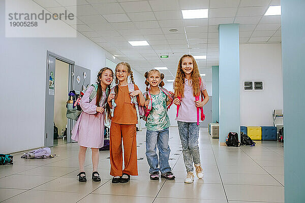Smiling school students standing together in school corridor