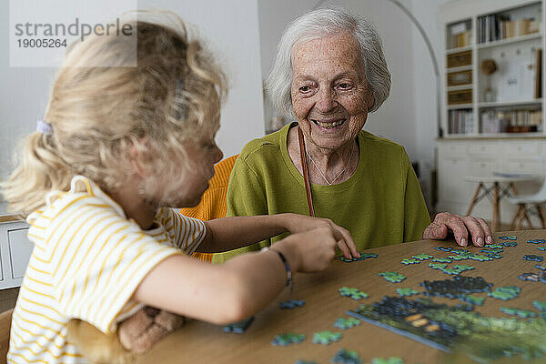 Lächelnde Großmutter schaut Enkelin beim Lösen eines Puzzles zu