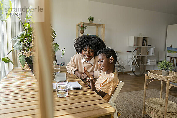 Glückliche Frau mit Sohn sitzt am Holztisch im Wohnzimmer