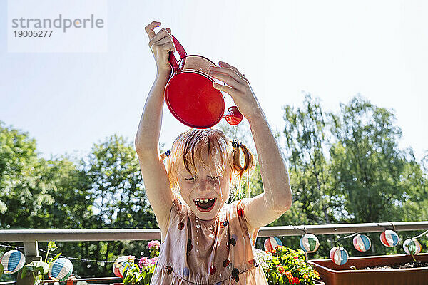 Fröhliches Mädchen gießt auf dem Balkon Wasser auf den Kopf