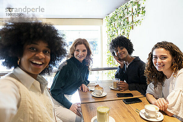 Glückliche junge Frau macht Selfie mit Freunden im Café