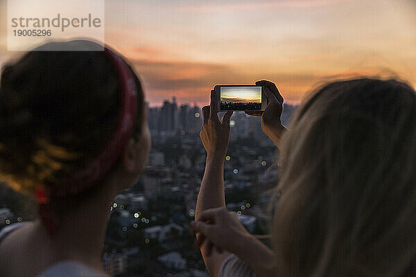 Freunde fotografieren in der Abenddämmerung den Blick auf die Stadt per Smartphone