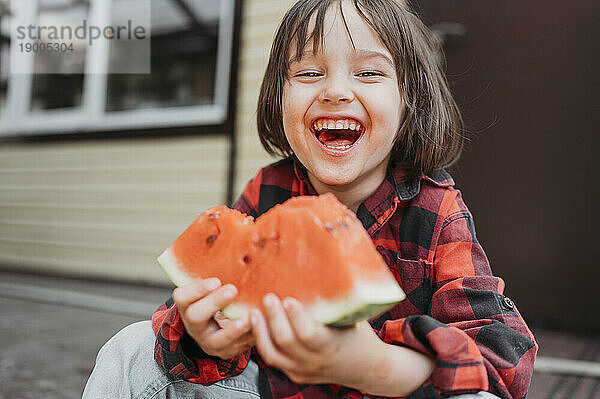 Fröhlicher Junge hält frische Wassermelonenscheibe