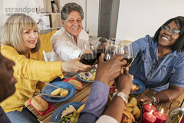 Fröhliche ältere  gemischtrassige Freunde  die bei einer Dinnerparty Weingläser anstoßen