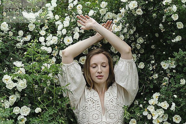 Junge Frau mit geschlossenen Augen und erhobenen Armen von einem weißen Blumenstrauch