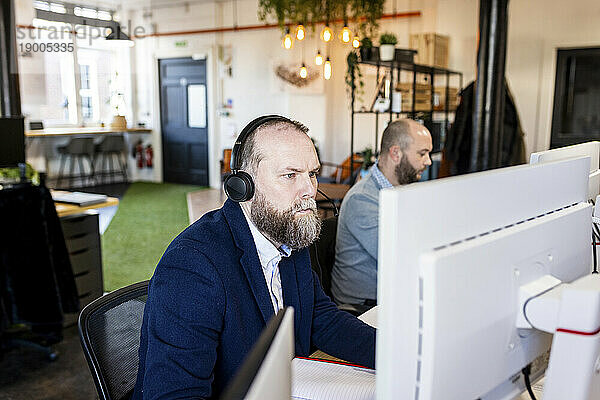 Reifer Geschäftsmann mit Headset  der im Büro am Computer arbeitet