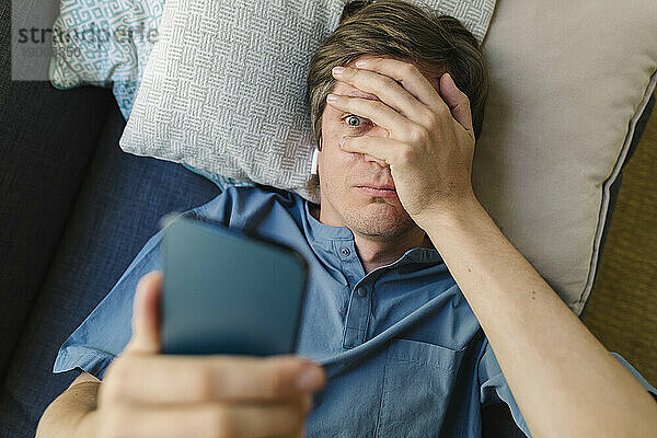 Besorgter Mann schaut auf sein Smartphone  das im Bett liegt