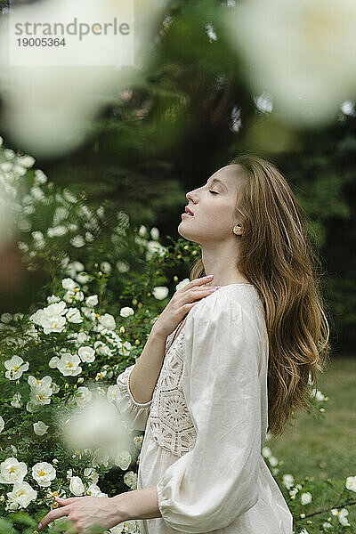 Junge Frau mit geschlossenen Augen steht neben einem weißen Blumenstrauch