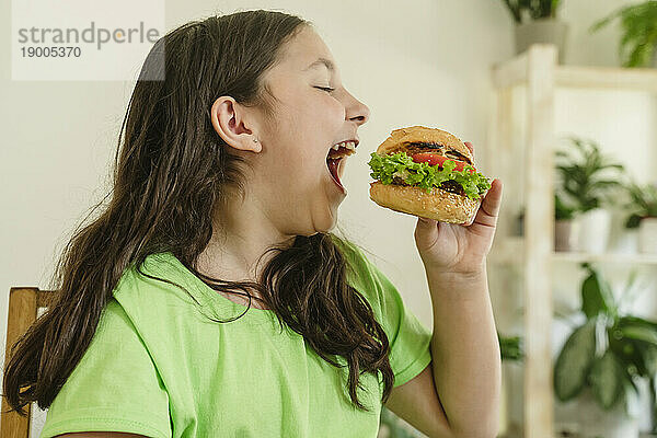 Glückliches Mädchen  das zu Hause Burger isst