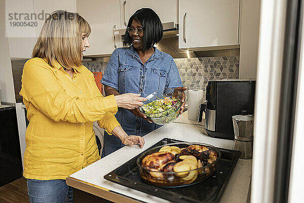 Ältere Frau hilft Freundin beim Zubereiten von Essen in der heimischen Küche