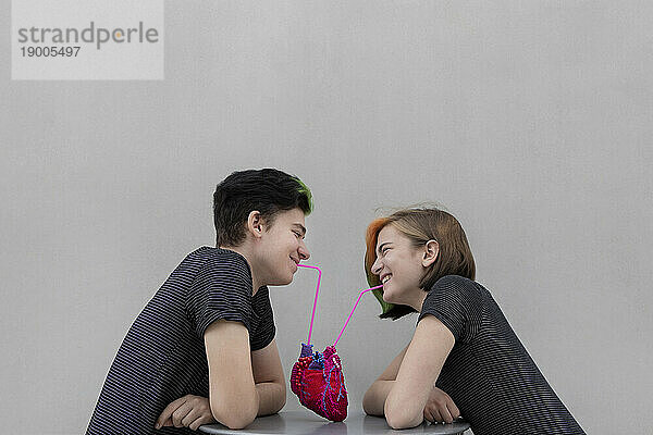 Fröhliches Teenager-Paar  das aus dem Herzen trinkt  vor grauem Hintergrund