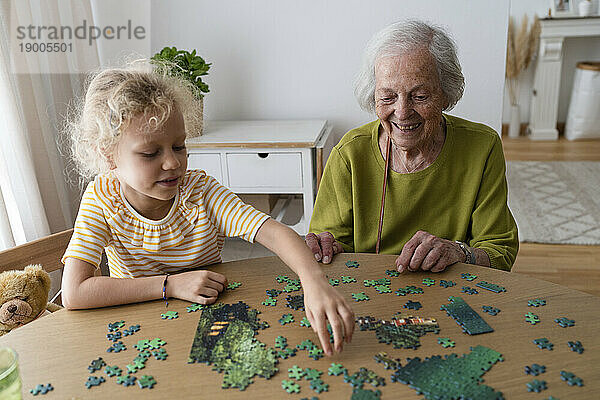 Lächelnde Großmutter und Enkelin lösen Puzzle