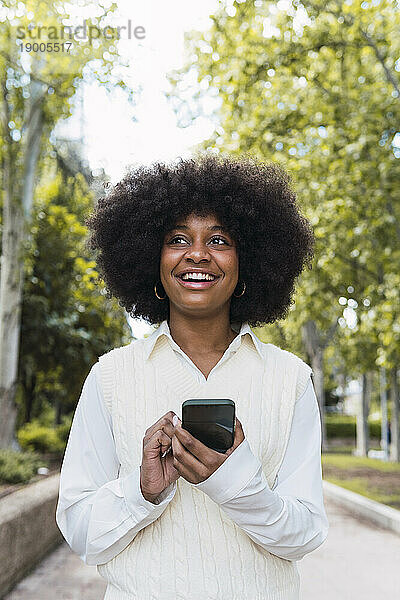 Glückliche Afro-Frau steht mit Smartphone im Park