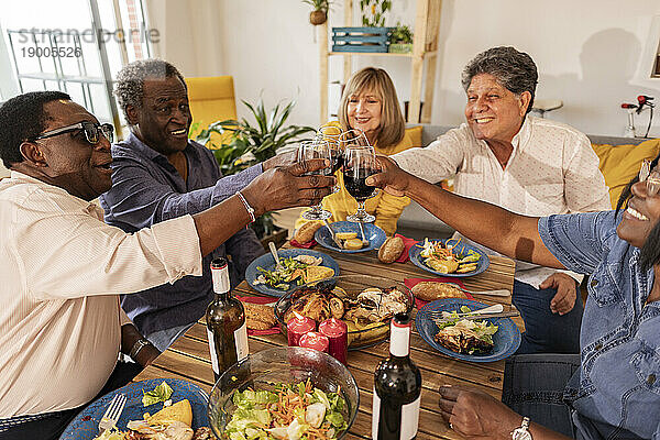 Multikulturelle ältere Freunde stoßen am Esstisch mit Weingläsern an