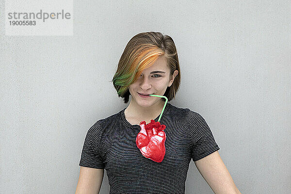 Teenage girl drinking from heart against gray background