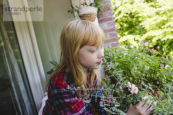 Blondes Mädchen riecht Pflanze auf dem Balkon