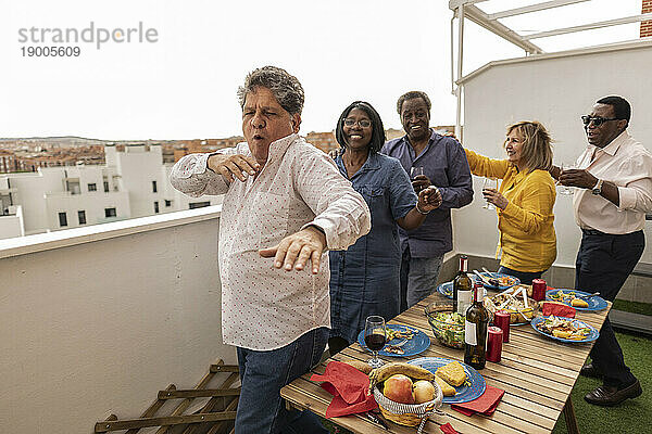 Älterer Mann tanzt mit Freunden bei Dinnerparty auf dem Balkon