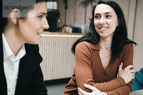 Lächelnde Geschäftsfrau diskutiert mit Bürofreundin im Café