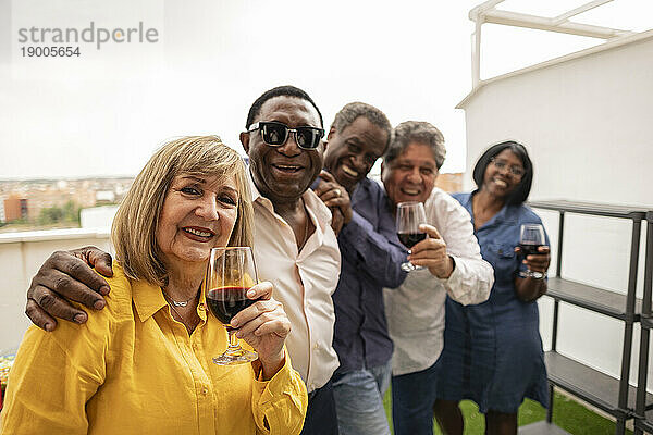 Lächelnde Frau hält Weinglas mit Freunden auf dem Balkon