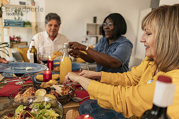 Smiling senior woman taking eating dinner with friends at home