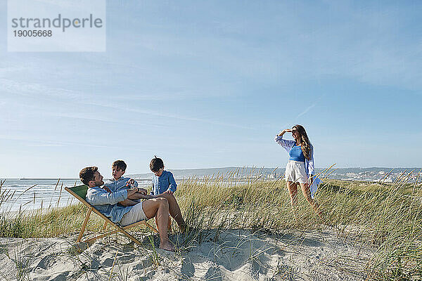 Mutter schaut Kinder an  Vater entspannt sich an sonnigem Tag am Strand